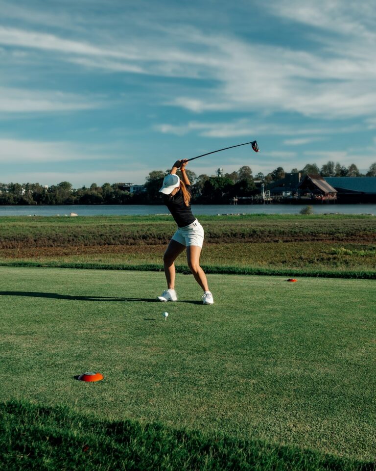 A golfer watches a ball flying toward the fairway, with a golf simulator screen in the background.