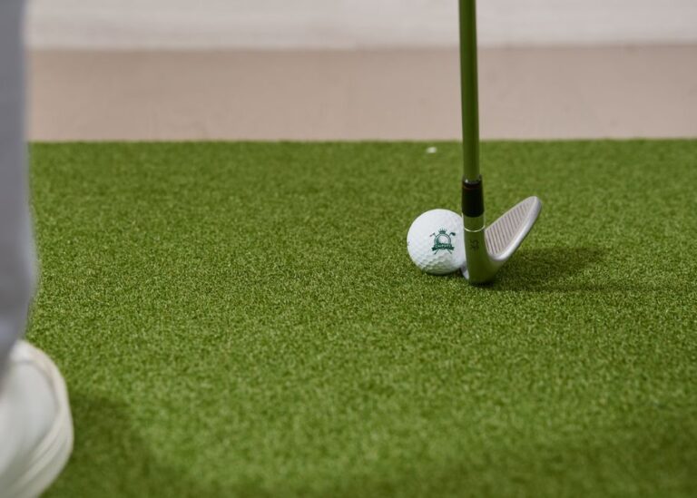 A young child swings a golf club at an indoor simulator under the supervision of a parent.