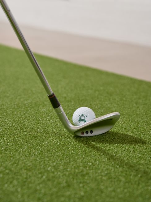 A golfer watches their own swing on a slow-motion video screen inside an indoor golf simulator bay.