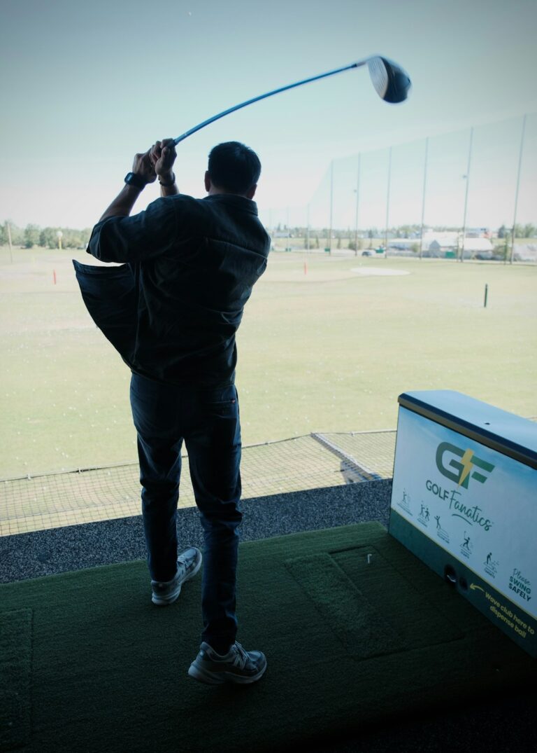 Golfer studies launch data beside a simulator screen while holding a club and reviewing shot results.