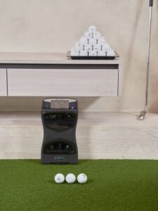 Golfer studies launch monitor numbers beside a club and ball on an indoor simulator mat.