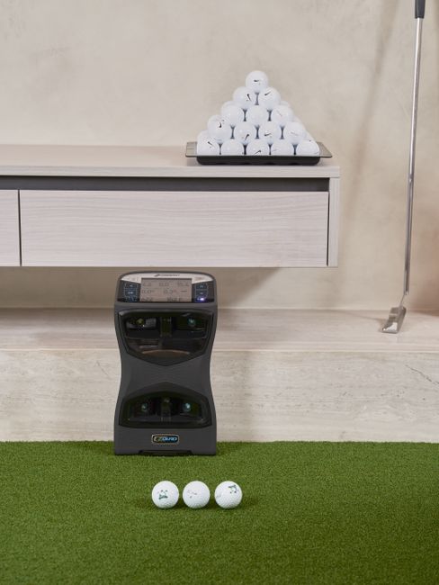 Golfer studies launch monitor numbers beside a club and ball on an indoor simulator mat.
